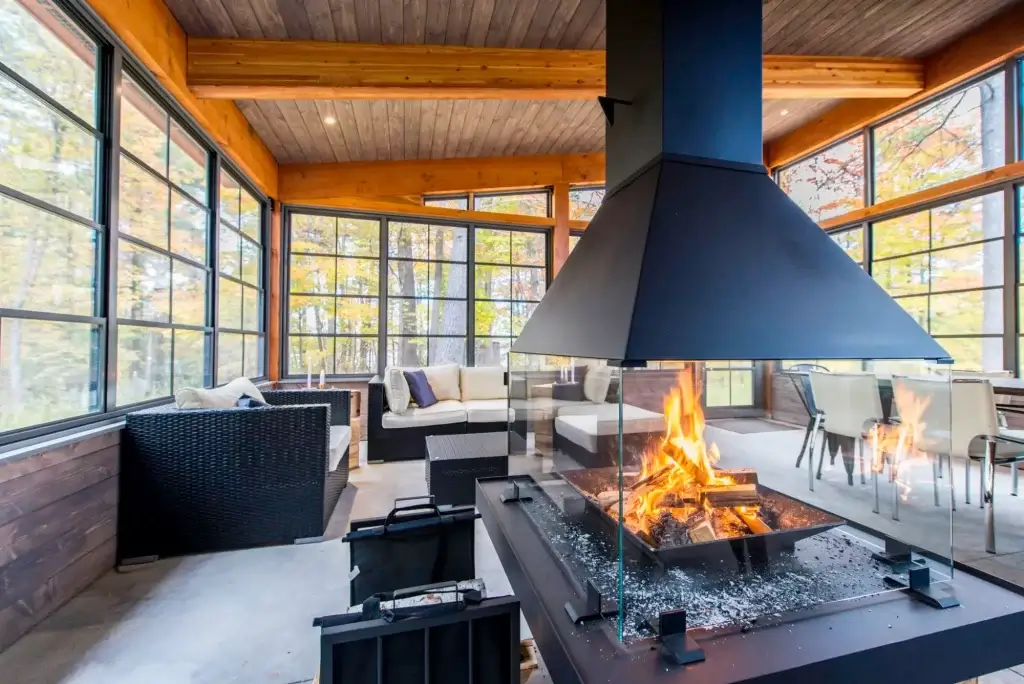 Modern Weather Master sunroom interior featuring central glass fireplace black furniture and autumn forest views