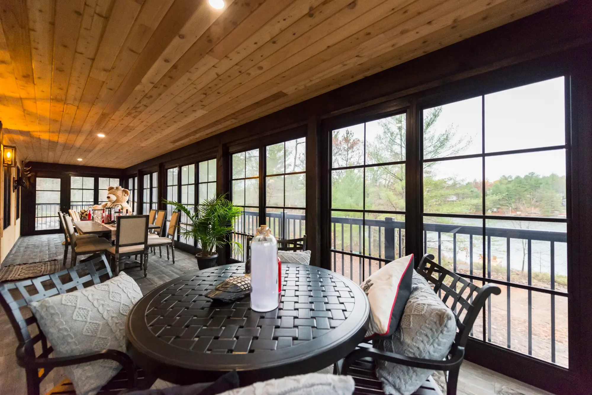 Interior view of an enclosed porch featuring black gridded windows, a natural wood ceiling, and a dining set