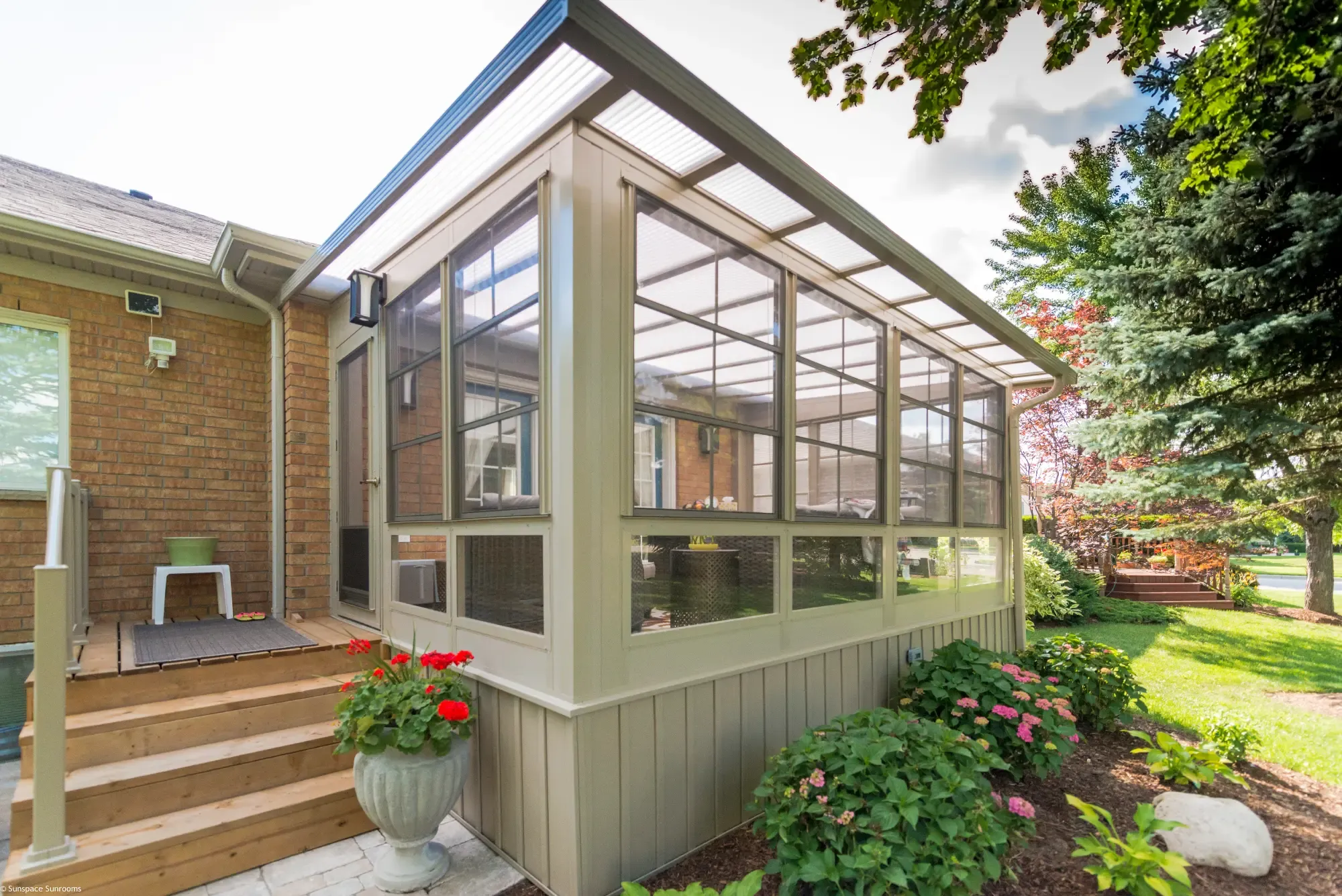 Exterior view of a Sunroom by NuBuild 3 season glass addition with a tan frame on a wooden deck