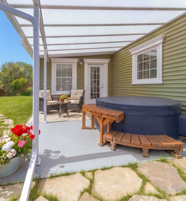White Sunspace NuBuild Beat the Heat patio cover over a concrete patio with a hot tub and wicker chairs