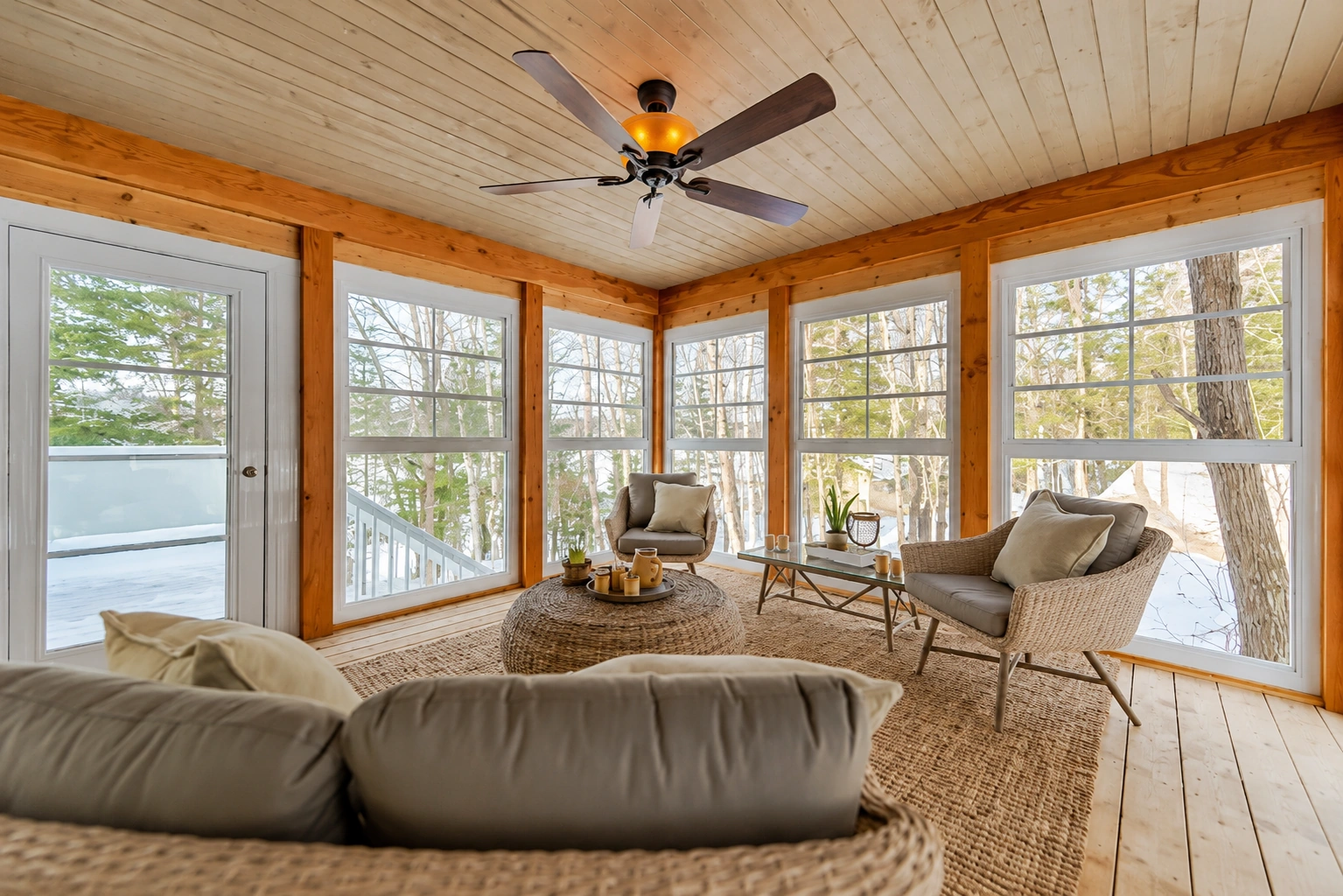 Enclosed sunroom featuring large windows, exposed wood beam trim, ceiling fan, and cozy seating