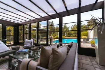 Modern dark framed sunroom interior with translucent roof panels overlooking an outdoor swimming pool