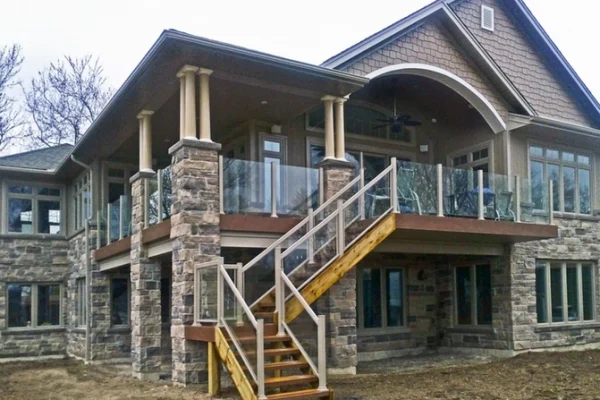 Topless glass railing system on an elevated deck with wooden stairs on a stone house
